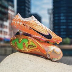 a pair of nike soccer cleats sitting on top of a cement block in front of a cityscape