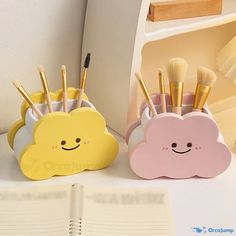 two small toothbrush holders sitting on top of a desk next to an open book