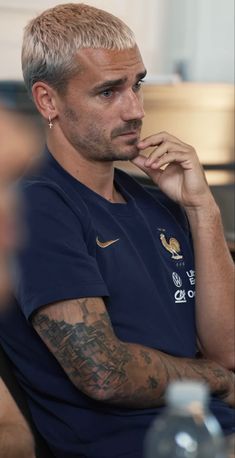 a man with tattoos on his arm sitting in front of a table and looking off to the side