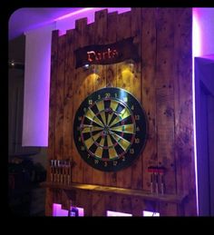 a dart board mounted to the side of a wooden wall with purple lights around it