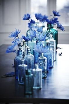 blue flowers are in glass bottles on a table