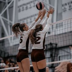 two girls playing volleyball in front of the net