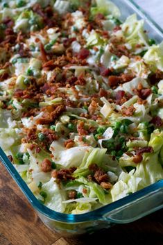 a glass casserole dish filled with lettuce, bacon and other toppings