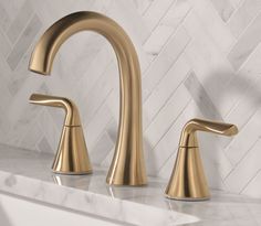 two gold faucets on a marble counter top