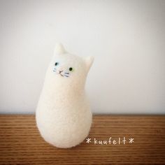 a white stuffed cat sitting on top of a wooden table next to a wall with the words kufflett written below it