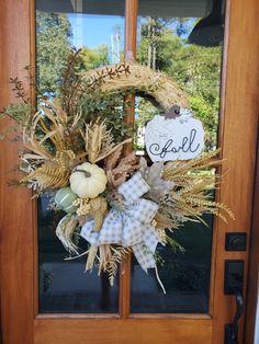 a wreath on the front door is decorated with pumpkins, wheat stalks and fall leaves