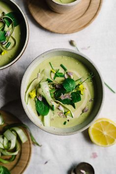 two bowls filled with green soup and garnished with fresh herbs, surrounded by sliced lemon wedges