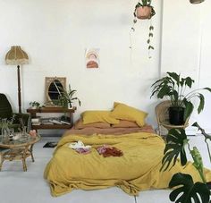 a bed with yellow sheets and pillows in a room filled with potted greenery