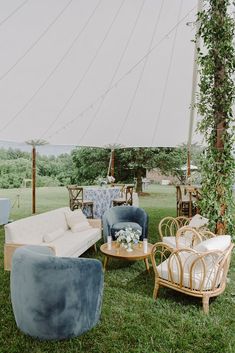 an outdoor seating area with wicker furniture and greenery on the grass, under a tent