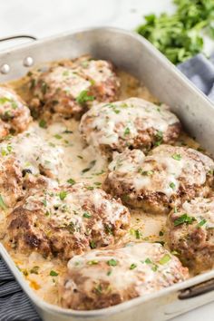 a casserole dish with meatballs covered in gravy and garnished with parsley