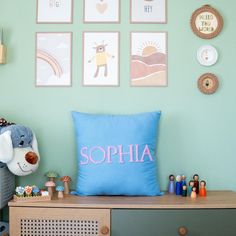 a blue pillow sitting on top of a wooden dresser next to a wall filled with pictures