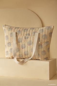 a beige bag sitting on top of a white box next to a pillow and headboard