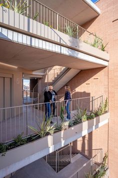 two people standing on the balcony of an apartment building with plants growing out of their balconies