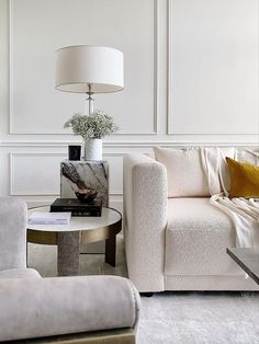 a living room filled with furniture and a lamp on top of a wooden table in front of a white wall