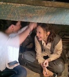 two people sitting on the ground in front of a fire place and one person reaching for something