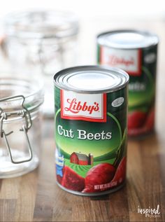 two cans of cut beets sitting on top of a wooden table next to glass jars