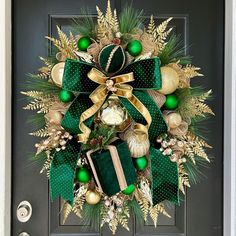 a green and gold christmas wreath on a black front door with ornaments hanging from it