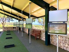 an outdoor golf course with benches and televisions on the wall, along with stone walls