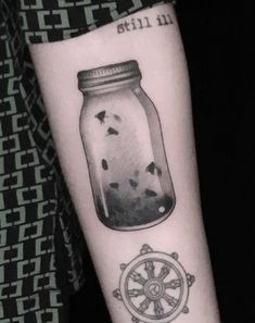 a person with a tattoo on their arm has a jar filled with seaweed and birds