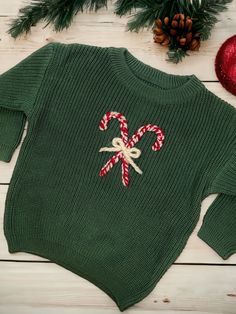 a green sweater with candy canes on it next to pine cones and christmas decorations