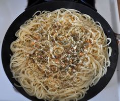 a pan filled with pasta and sauce on top of a white countertop next to utensils