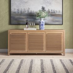 a painting hanging on the wall above a wooden cabinet with wine glasses and vases