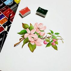 some watercolors are sitting on a table next to a painting with pink flowers and green leaves