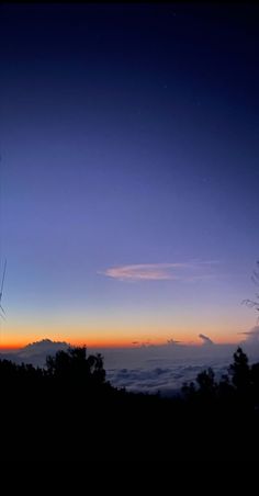 the sun is setting over the clouds in the sky with trees and bushes around it