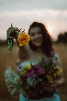 a woman holding a bouquet of flowers in front of her face with the sun setting behind her