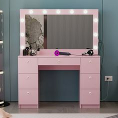 a pink vanity with lights on it and a mirror in the corner next to it