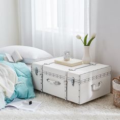 a white suitcase sitting on top of a bed next to a vase with flowers in it