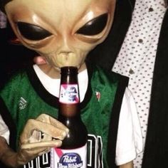 an alien holding a beer bottle in its mouth