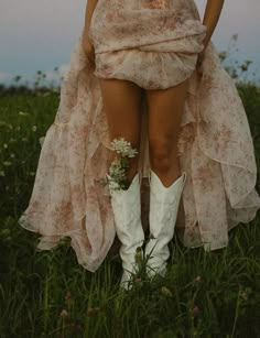 a woman wearing white cowboy boots and a pink dress sitting in the middle of a field