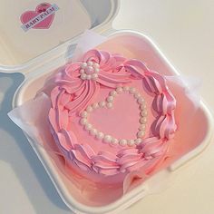 a heart shaped cake in a plastic container with pink ribbon and pearls on the top