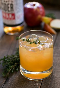 an apple cider sits on a wooden table next to apples