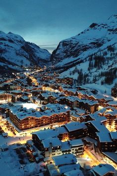 an aerial view of a town in the mountains at night with snow on the ground