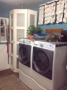 a cat laying on top of a washing machine in a room with blue walls and white cabinets