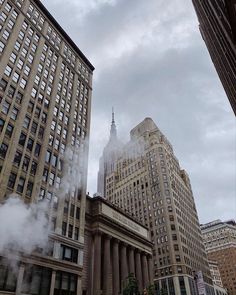 steam rises from the ground in front of tall buildings on a cloudy day with no clouds