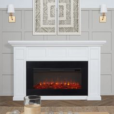 an electric fireplace in a living room with two pictures on the wall above it and candles