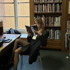 a woman sitting on a chair reading a book in front of a library full of books