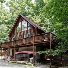 a log cabin in the woods with a red car parked on the driveway and stairs leading up to it