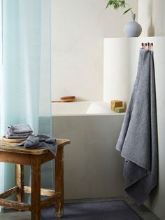 a towel is hanging on a rack next to a bathtub and wooden stool in a bathroom