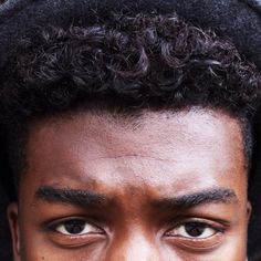 a close up of a person wearing a black hat and holding a cell phone to his ear