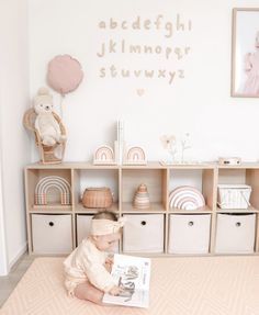 a baby is sitting on the floor in front of a bookcase with letters and toys