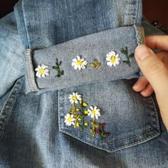 someone is stitching daisies on the back of their jean jacket