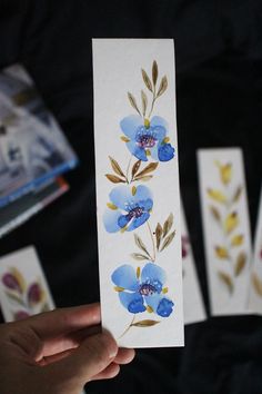 a person holding up a piece of paper with watercolor flowers on it and four other cards in the background