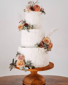 a three tiered white cake with flowers on the top and sides is sitting on a wooden stand