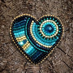 a heart shaped brooch sitting on top of a piece of wood with beading