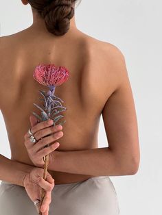 a woman holding a pink flower in her right hand and looking down at the back