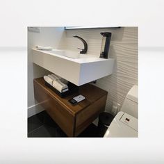 a white sink sitting on top of a wooden table next to a toilet and paper towel dispenser